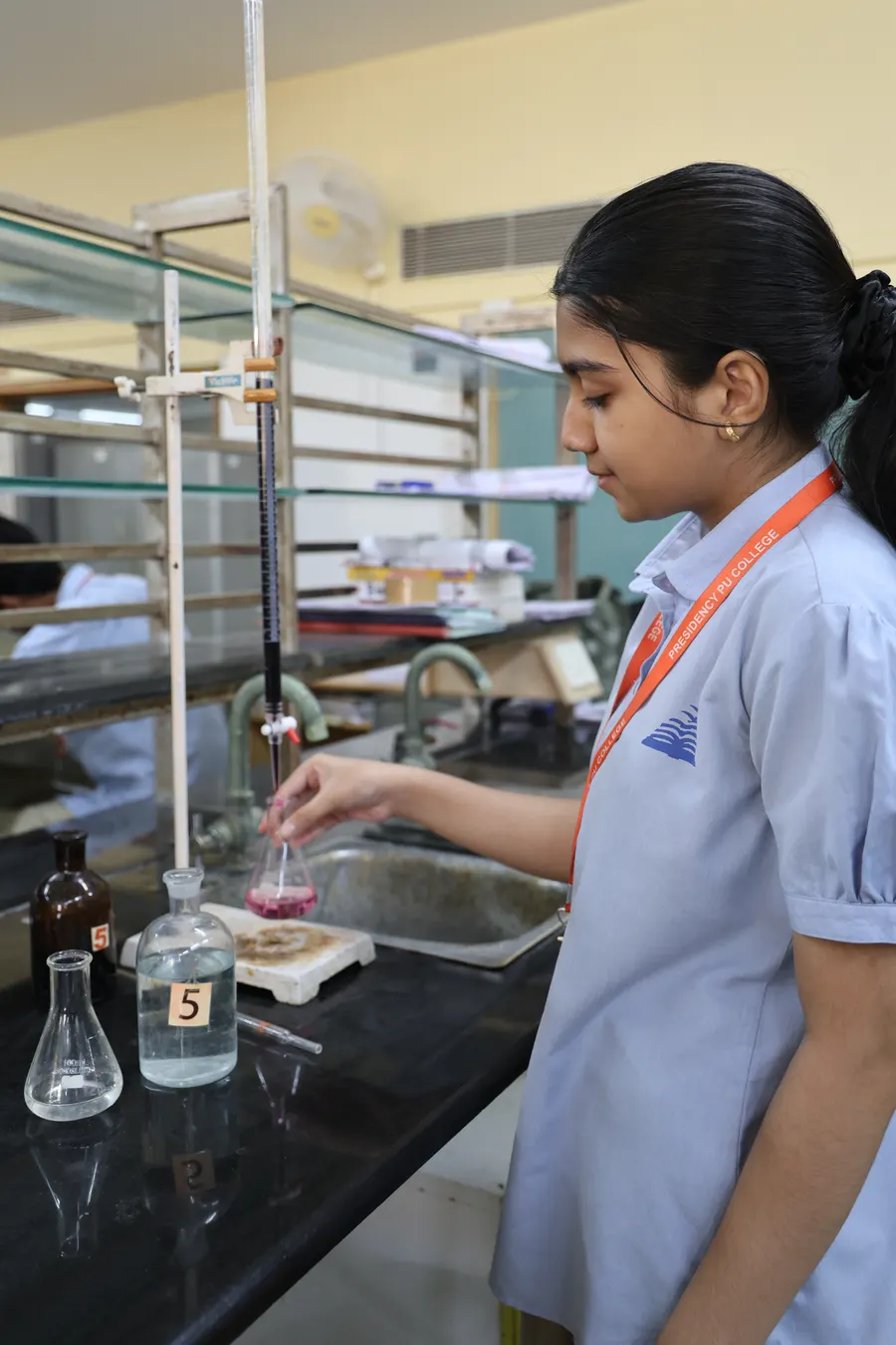 A student in the chemistry lab, titrating a pink solution into a flask.