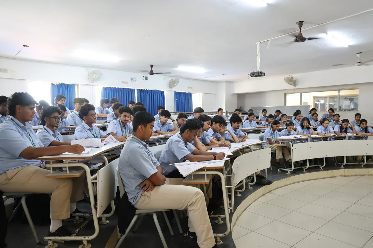 A classroom with curved tiered desks, students seated and writing.