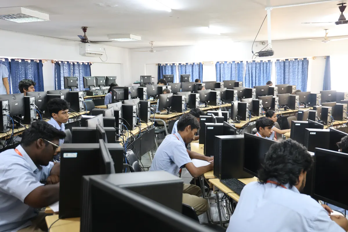 A student at work in the computer lab, rows of desktops behind him.