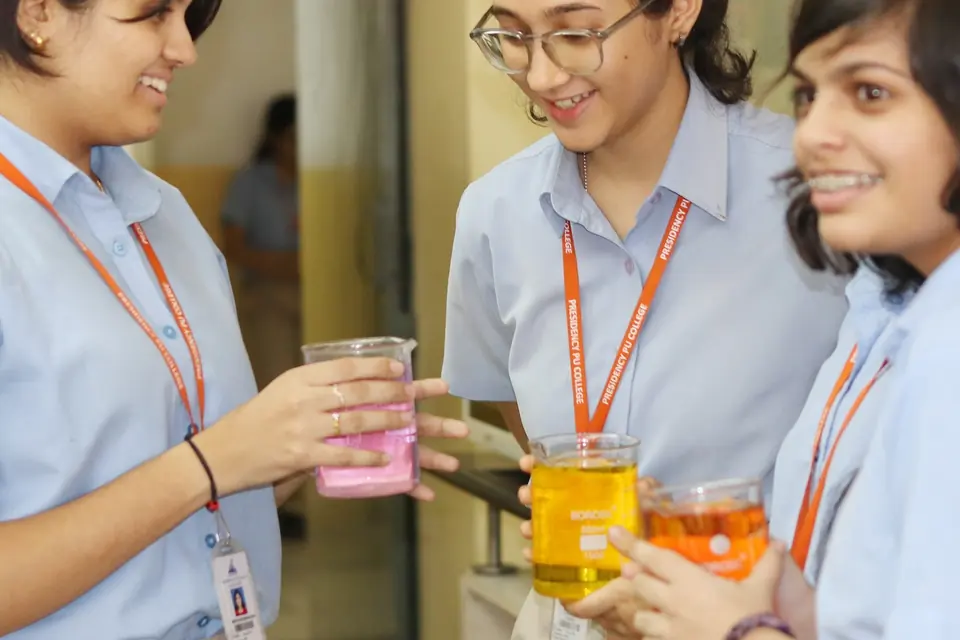 Three students in the chemistry lab holding beakers of coloured solutions.
