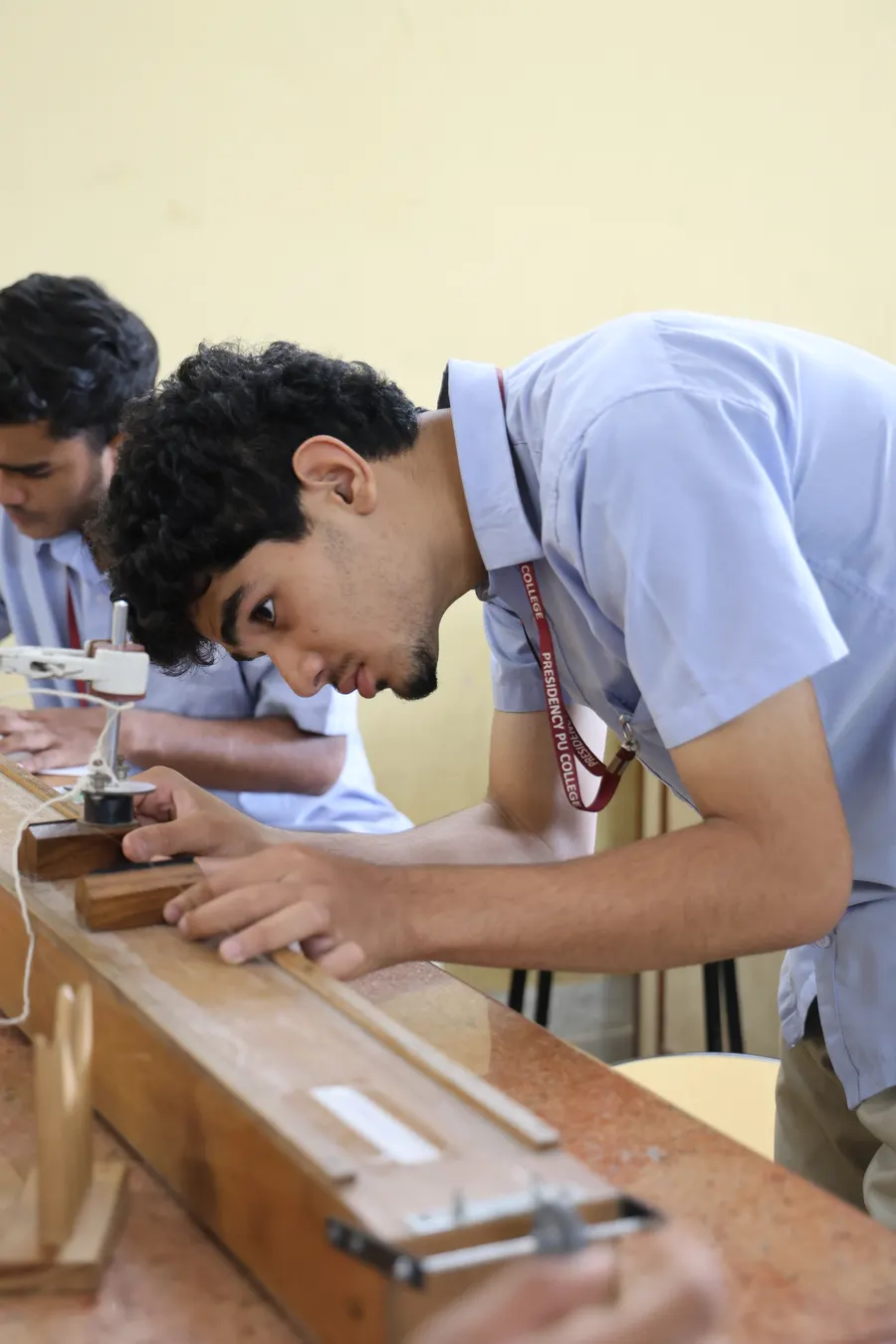 A student adjusting a wooden apparatus at the physics lab bench.