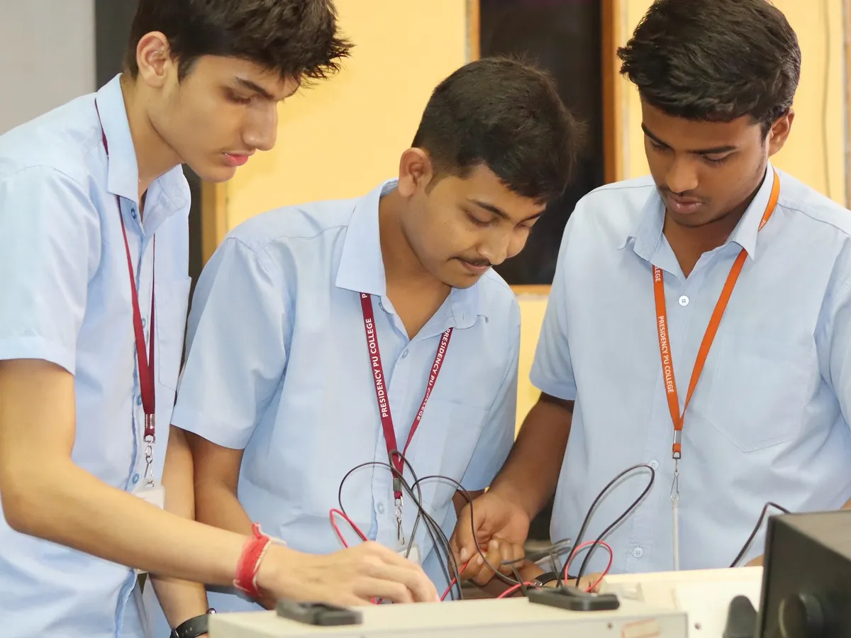 Three Presidency PU students in the physics lab, wiring a circuit on a bench together.