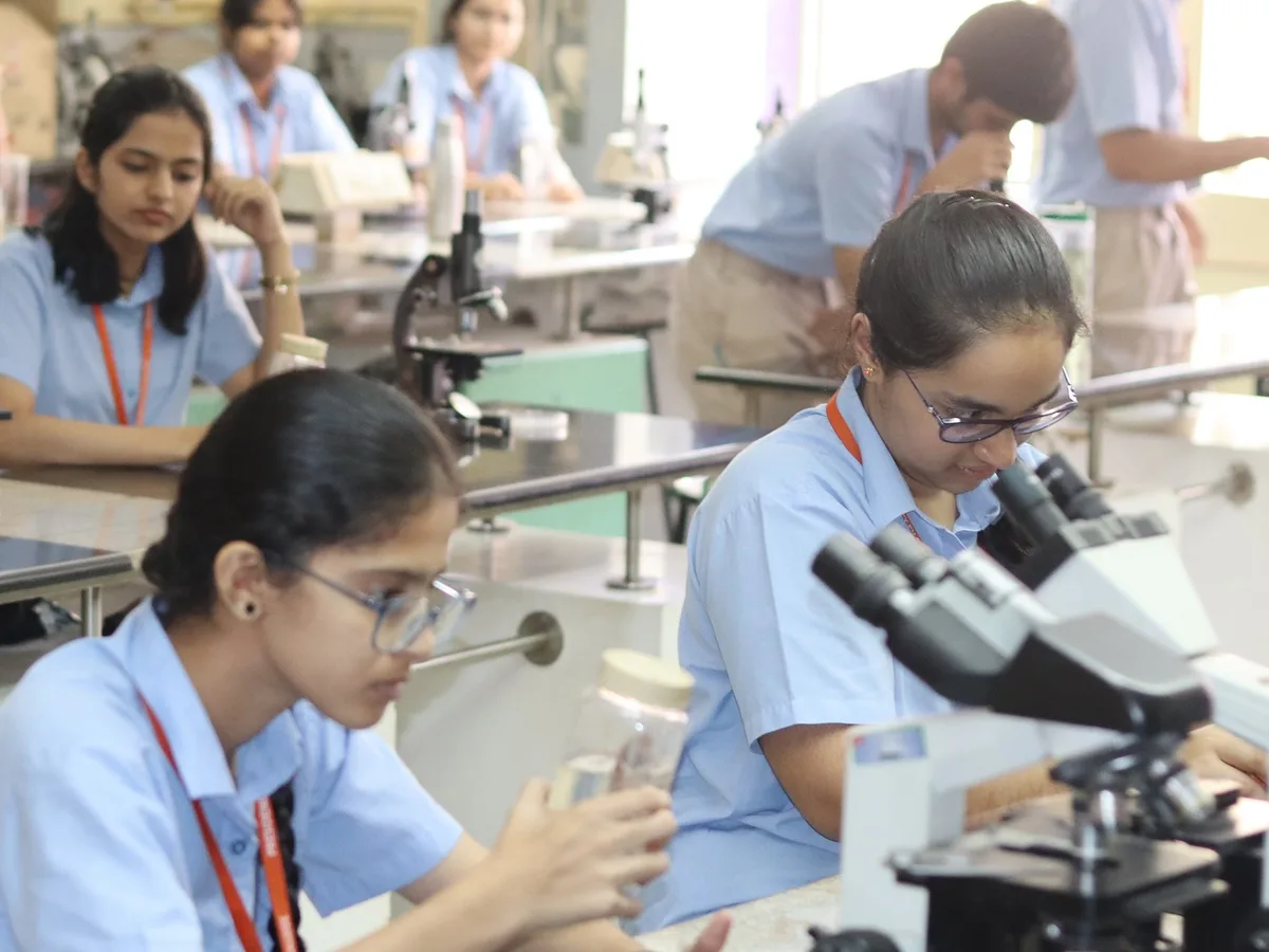 Two students at a microscope bench in the Biology lab, with classmates working behind them.
